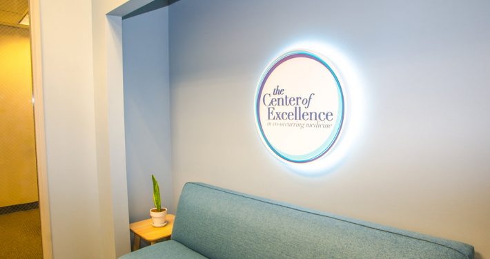 center of excellence waiting room with their lit up logo on the wall
