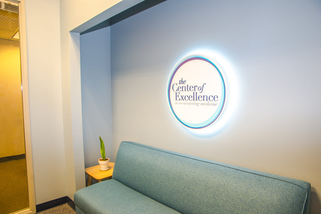 center of excellence waiting room with their lit up logo on the wall
