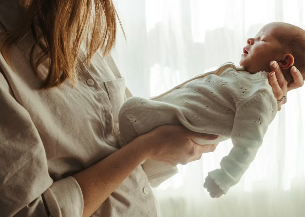 Mother holding a baby in the morning next to window